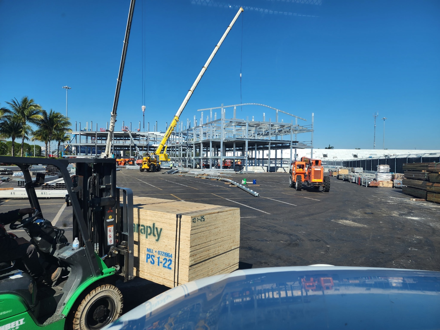 Forklift and flatbed truck delivering lumber at large event construction site in Miami