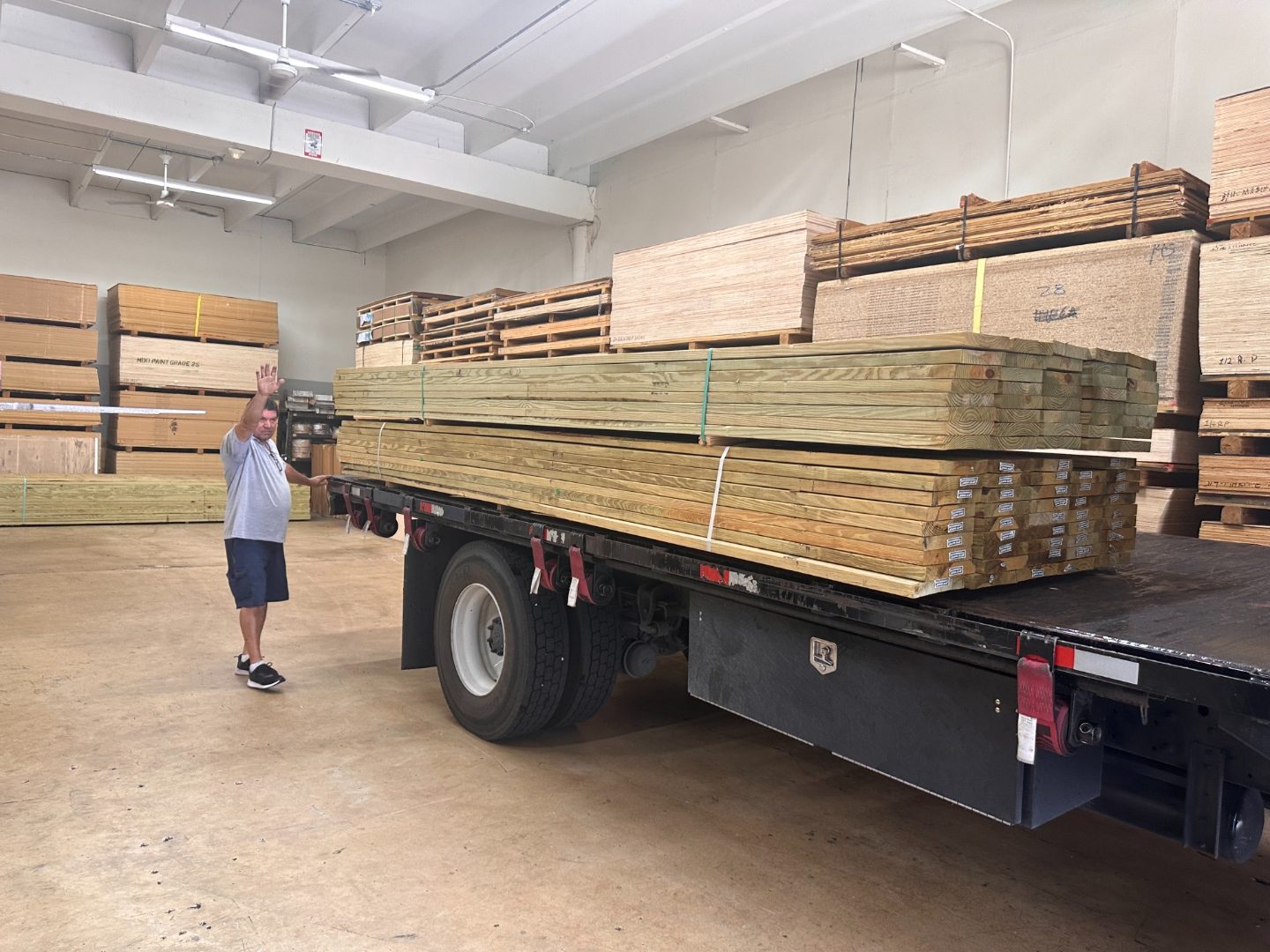 Employee waving next to flatbed truck loaded with pressure treated lumber bundles inside International Plywood warehouse