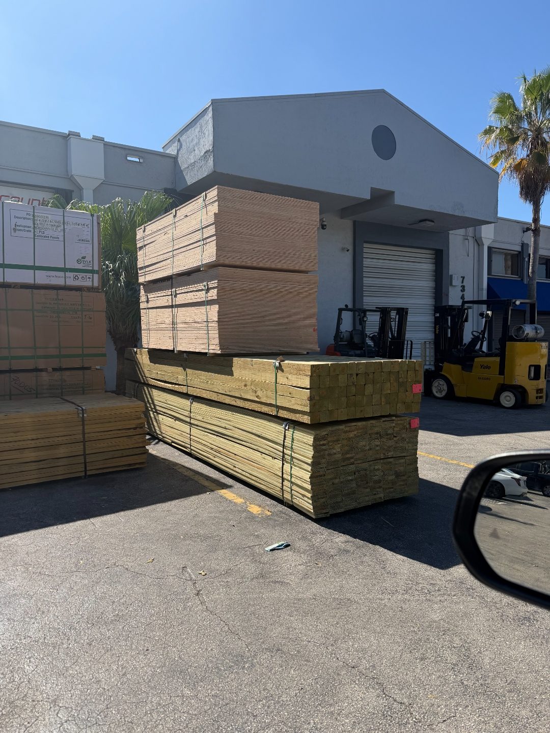 Pressure treated lumber and plywood stacks outdoors with Yale forklifts and blue sky